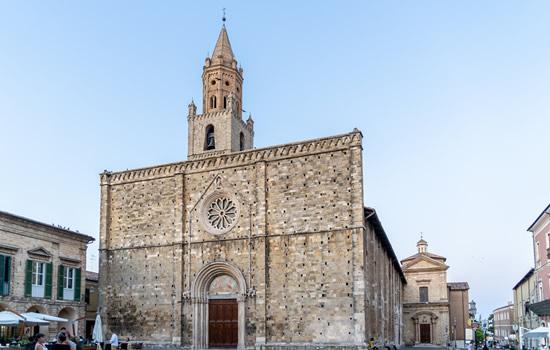 Imponente chiesa medievale in pietra, con rosone e alto campanile.